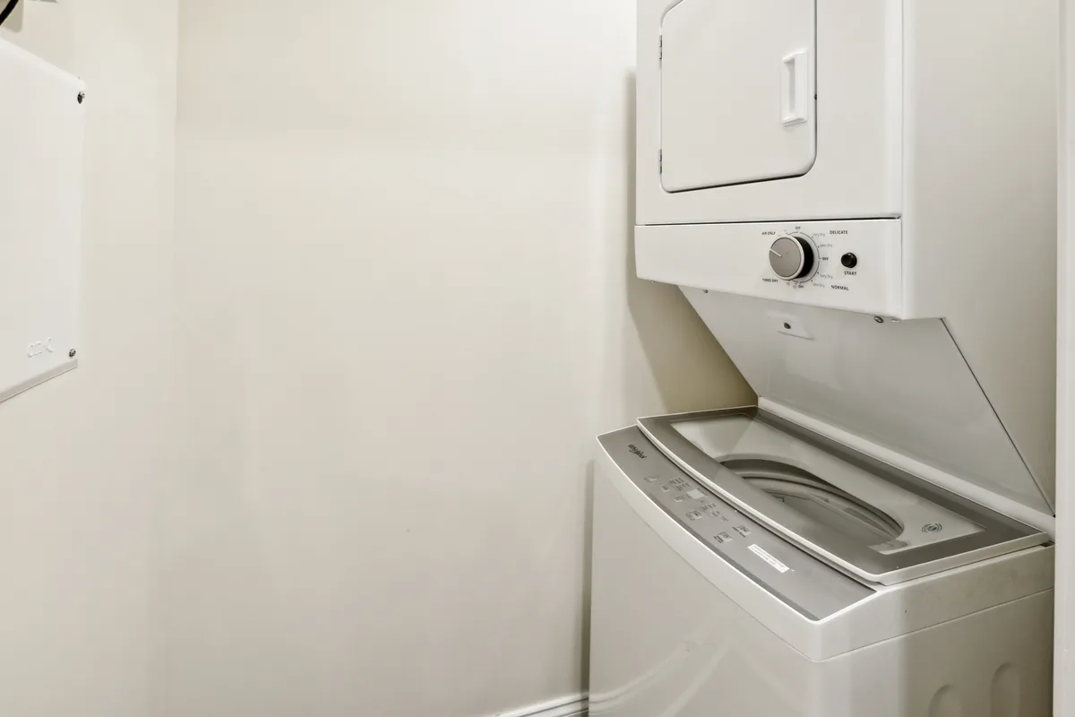 A light, practical space featuring a washer and dryer along light-colored walls. The area appears efficient for household tasks and is positioned near what could be a main hallway, helping illustrate the convenience and turn-key living described in the section.