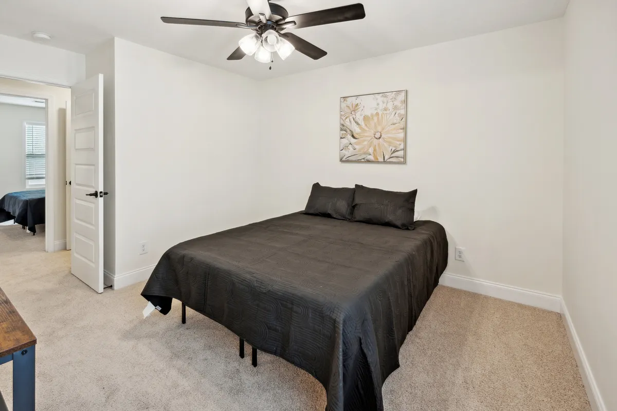 This image features a serene bedroom with black bedding, a ceiling fan, and tasteful wall art. The space exudes peacefulness and provides a comfortable retreat ideal for rest and relaxation after a day spent exploring the local area.