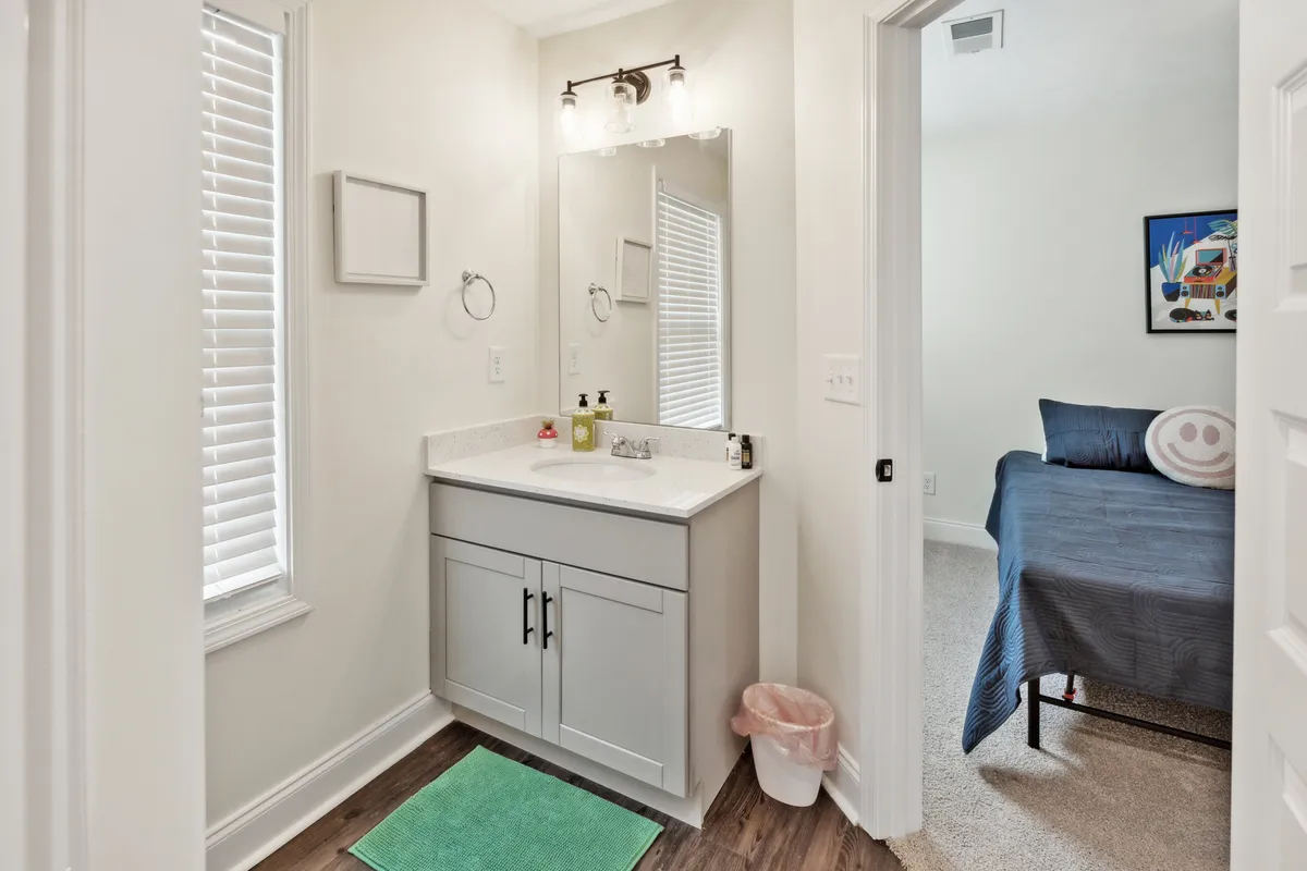 A well-lit bathroom vanity with a large mirror, window blinds for natural light, and a glimpse of colorful artwork in an adjacent room. The space feels fresh and welcoming, offering a practical spot for family routines.